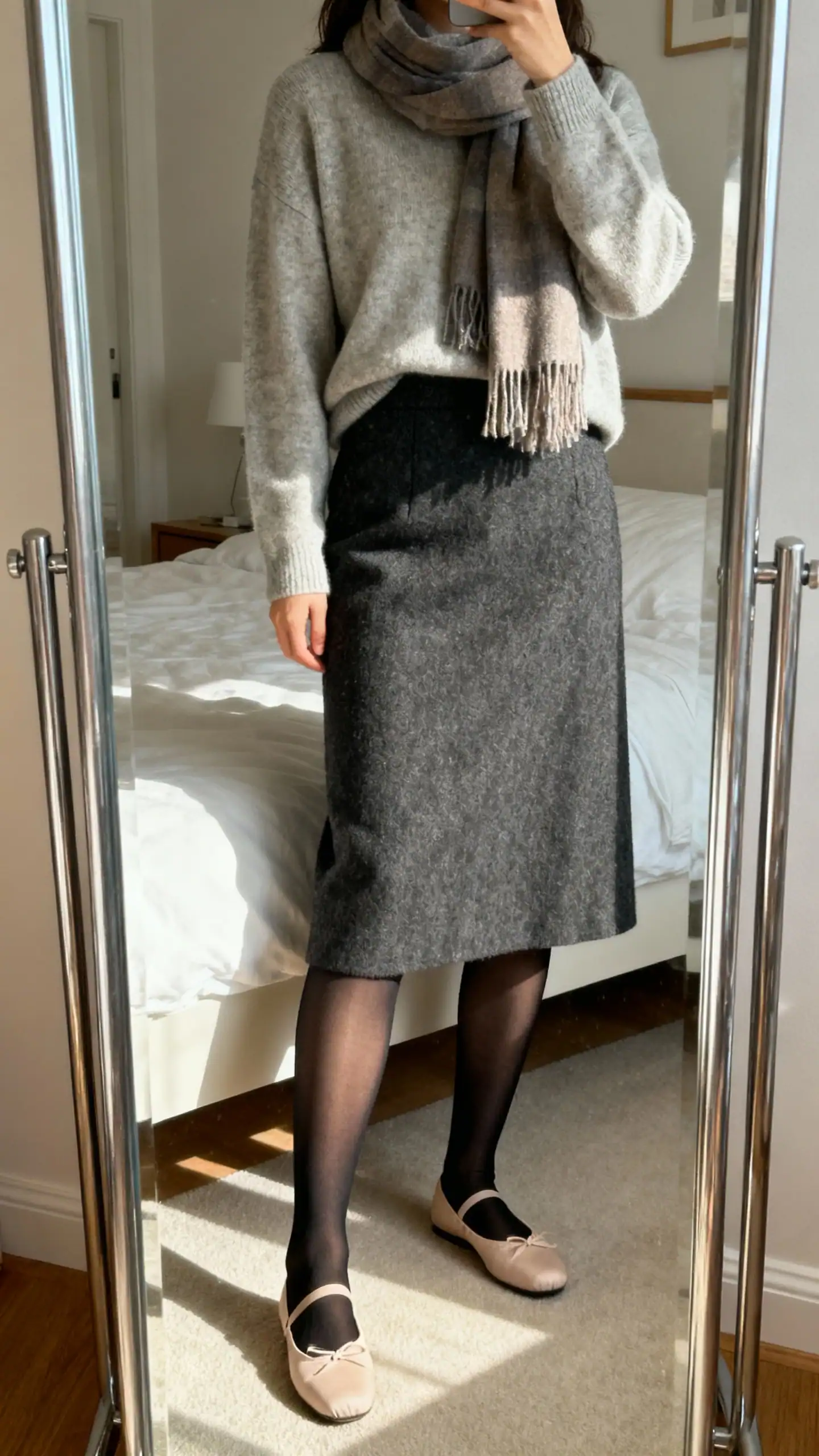 iPhone mirror selfie of a woman in semi-opaque black tights, ballet flats, and a wool midi skirt with a simple sweater and scarf, face not visible, cropped at shoulders in a bedroom mirror, soft morning light, iPhone photo quality.