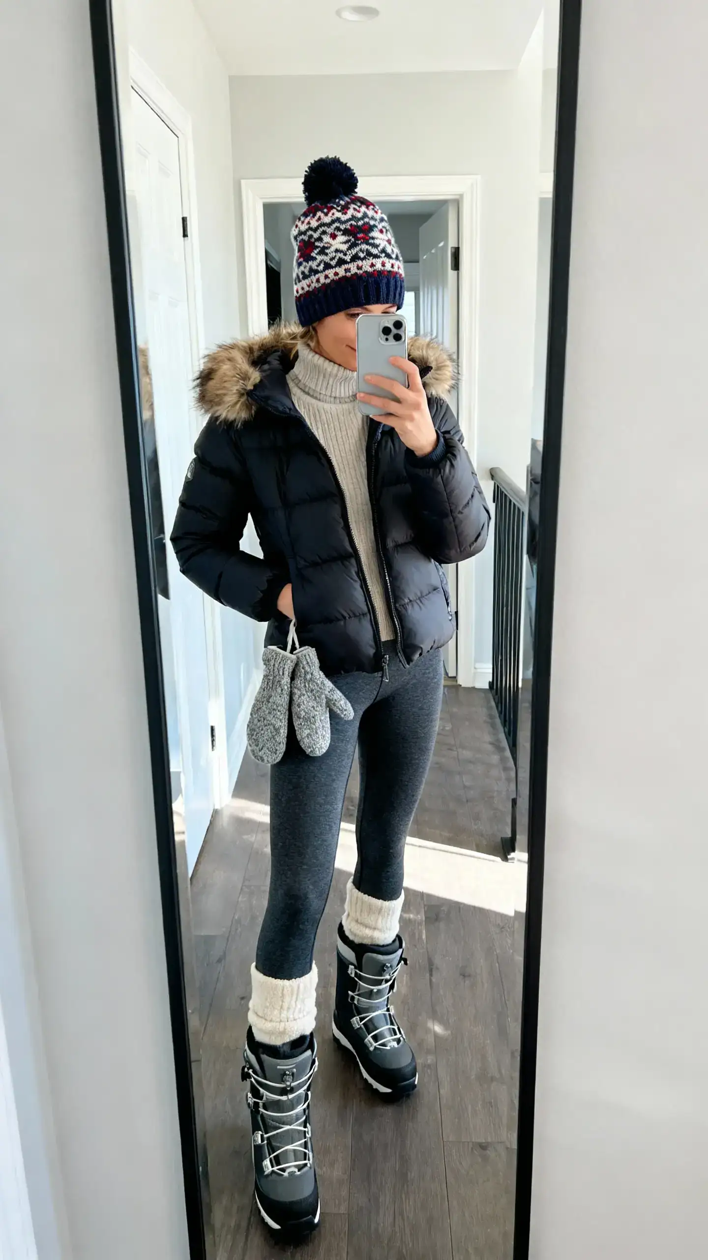 iPhone mirror selfie of a woman wearing a chunky fair isle beanie, faux-fur trim puffer jacket, cashmere turtleneck, fleece-lined leggings, apr&egrave;s-ski snow boots, and wool mittens tucked in pocket, face not visible, entryway full-length mirror, cool daylight, iPhone photo quality.