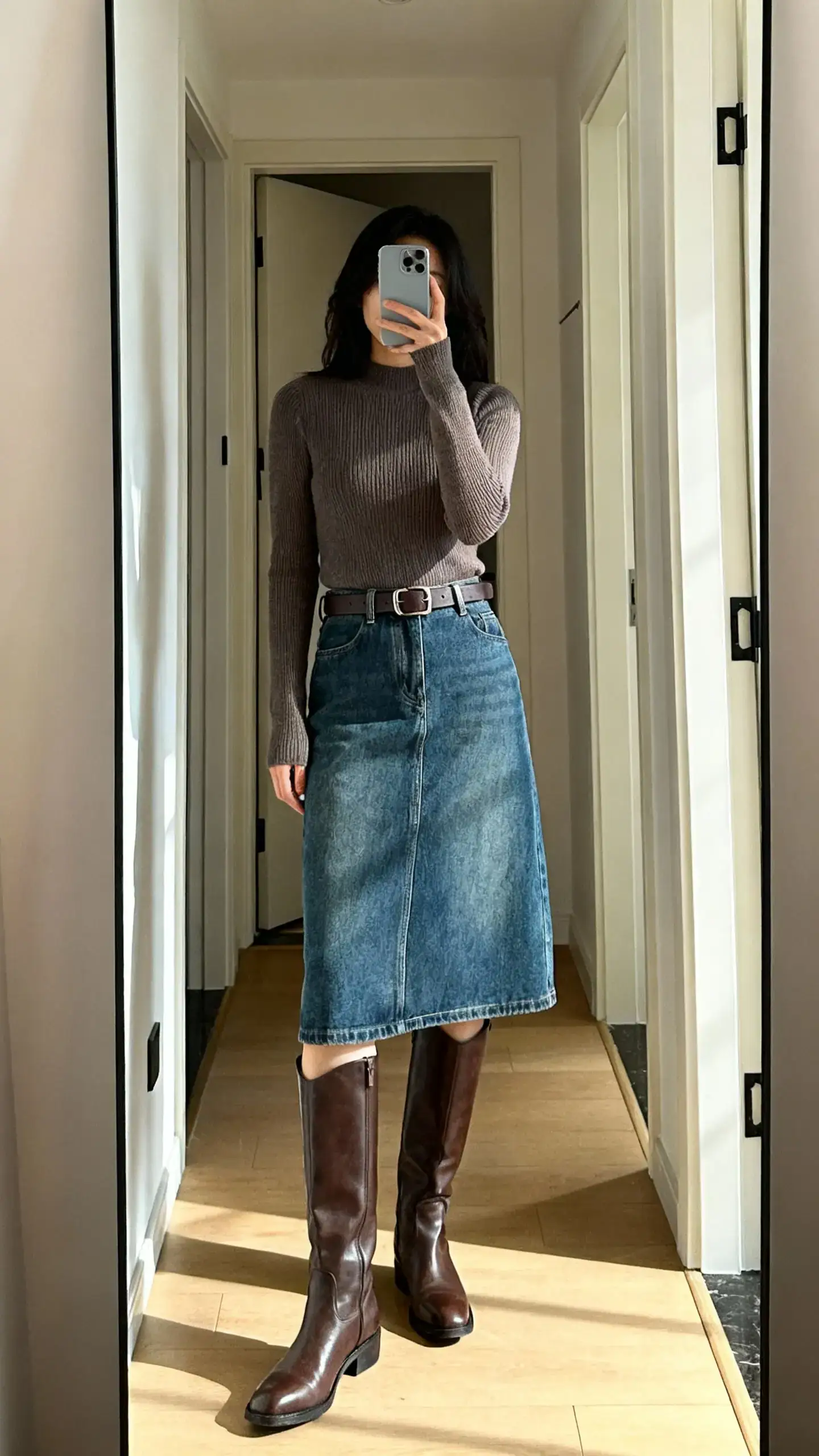 iPhone mirror selfie of a woman wearing a denim midi skirt with tall leather boots, a fitted sweater and a belt, face not visible, entryway full-length mirror, natural daylight, iPhone photo quality.