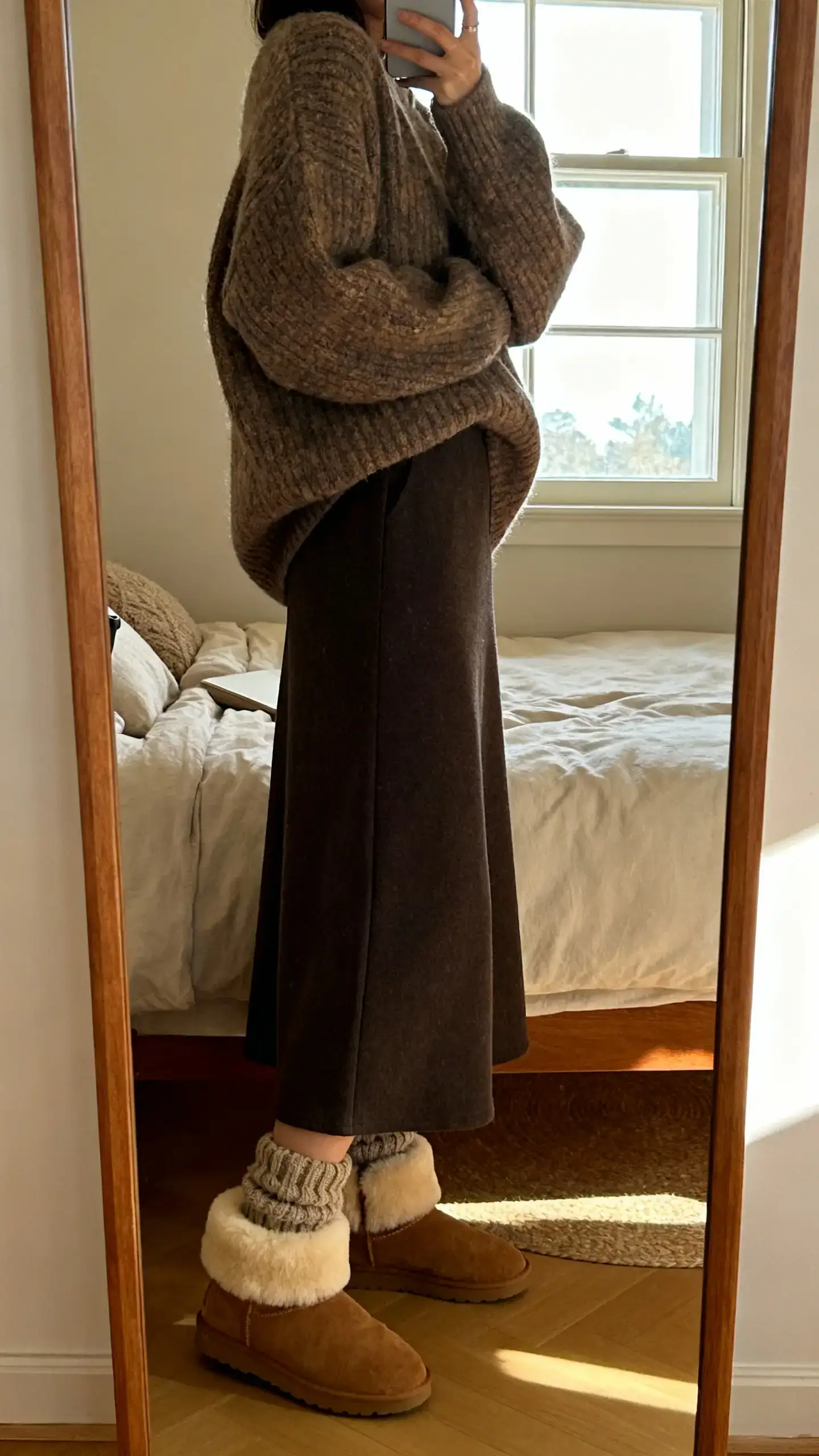 iPhone side-angle mirror selfie of a woman wearing a maxi skirt with shearling-lined boots, chunky socks peeking and an oversized knit, face not visible, full-length mirror in a cozy bedroom, window light, iPhone photo quality.
