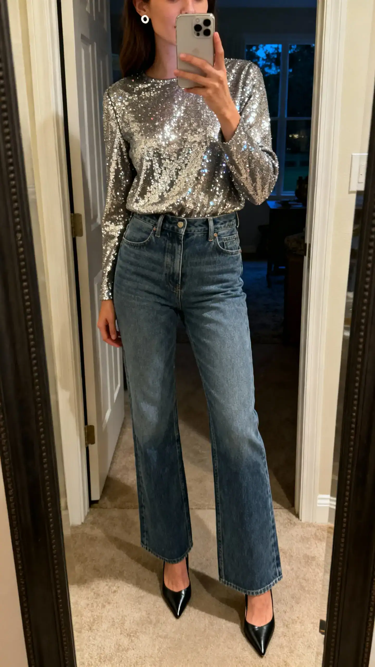 iPhone mirror selfie of a woman in high-rise denim with a sparkle top (sequined or metallic) and pointed-toe heels, simple stud earrings, face not visible, full-length mirror in entryway, evening indoor light, iPhone photo quality.