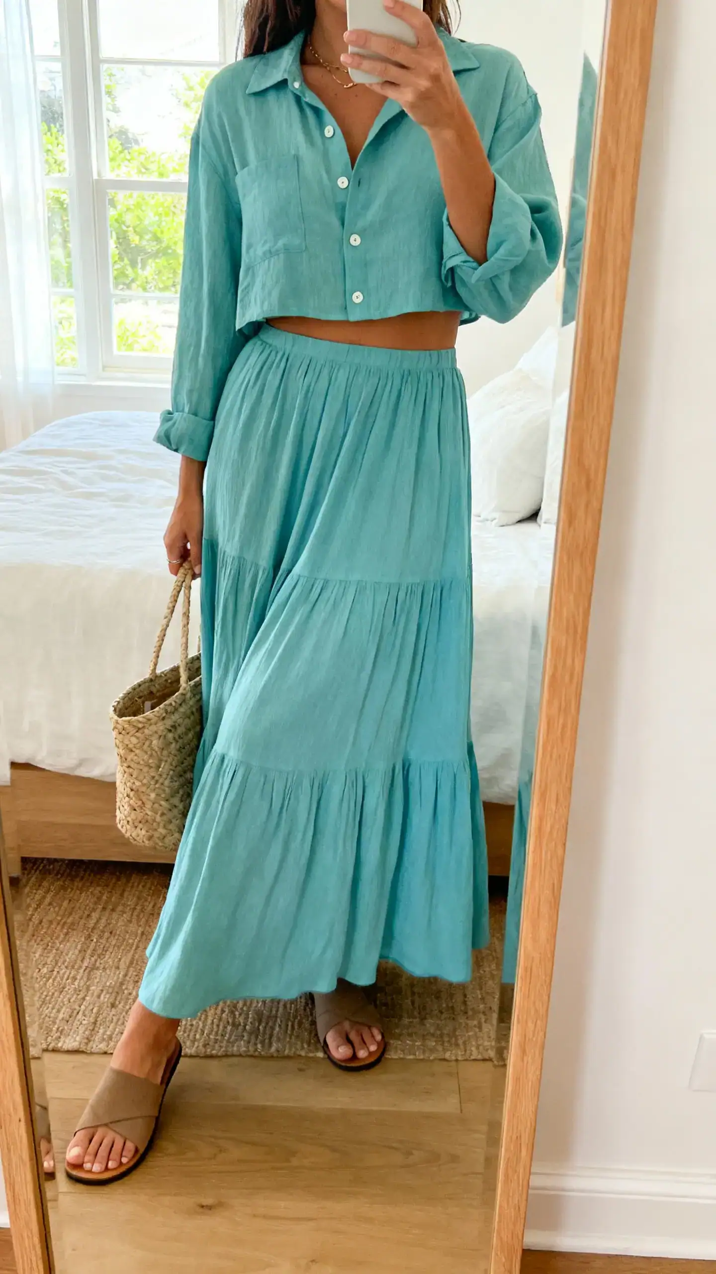 iPhone side-angle mirror selfie of a woman wearing a coastal co-ord set: cropped button-down shirt and matching flowy maxi skirt, with flat sandals and a woven tote, face not visible, bedroom mirror, natural window light, iPhone photo quality.